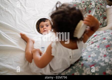 La ragazza (2-3) pettinare capelli sul letto con specchio Foto Stock