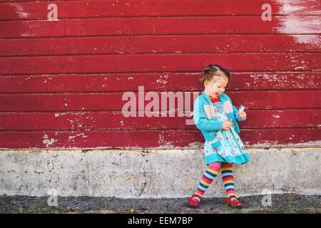 Ragazza felice in piedi da una parete rossa che tiene una piuma, Stati Uniti Foto Stock