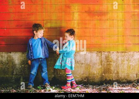 Ragazzo e ragazza in piedi da un muro che tiene le mani Foto Stock