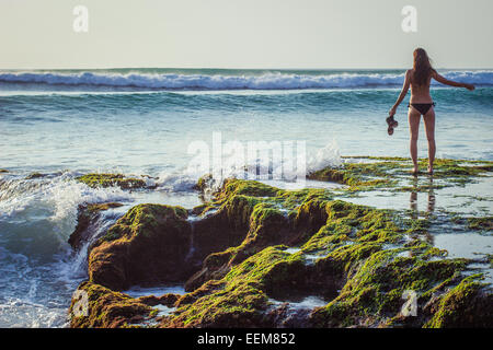 Donna in piedi su rocce al mare, Bali, Indonesia Foto Stock