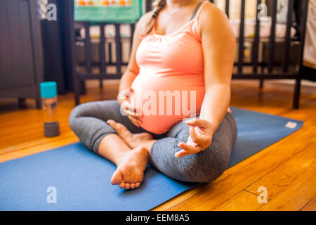 Incinta donna caucasica meditando in vivaio Foto Stock