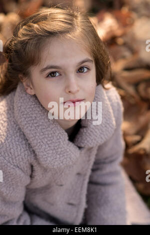 Ragazza carina (8-9) seduto in foglie di autunno Foto Stock