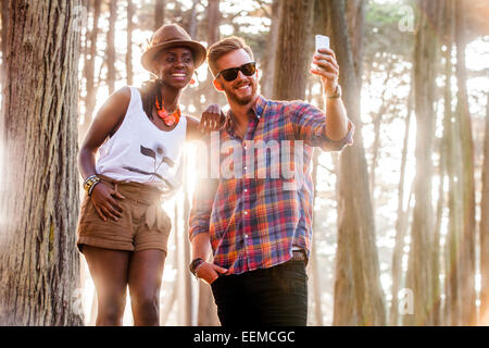 Giovane tenendo cellulare foto nella foresta di sole Foto Stock