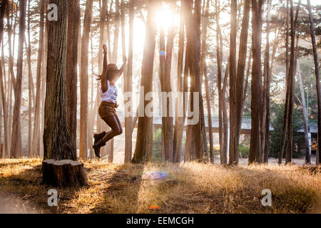 Nero donna jumping dal moncone nella foresta di sole Foto Stock