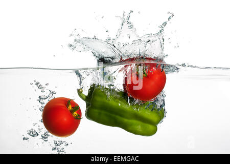 Primo piano di pomodori freschi e pepe verde cadere in acqua chiara con grande splash isolati su sfondo bianco Foto Stock