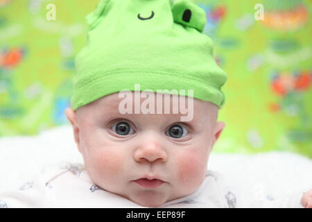 Blue eyed Caucasian baby boy indossando una rana verde hat Foto Stock