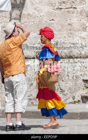 Donna locale in vivacemente colorato abito in cerca di consigli e la vendita di fiori in piazza del Duomo, Avana Vecchia, parlando ad un turista Foto Stock