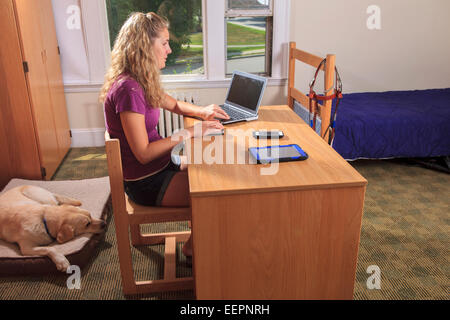 Studente con minorazione visiva utilizzando il suo computer parlando nella sua stanza con il suo cane di servizio Foto Stock