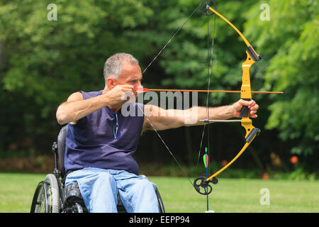 Uomo con lesioni al midollo spinale in carrozzella mirando il suo arco e la freccia per la pratica del tiro con l'arco Foto Stock