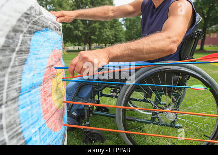 Uomo con lesioni al midollo spinale in carrozzella rimozione frecce dal bersaglio dopo la pratica di tiro con l'arco Foto Stock