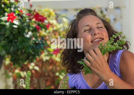 Donna con la Spina Bifida annusare le erbe in un giardino fiorito Foto Stock