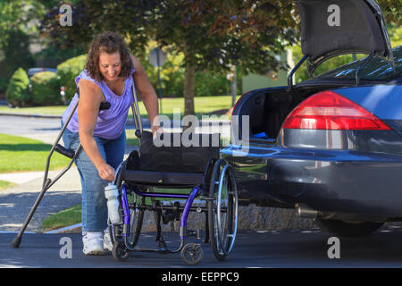 Donna con la Spina Bifida smontaggio di sedia a rotelle per metterlo nella parte posteriore della macchina Foto Stock