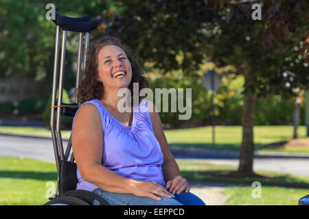 Donna con la Spina Bifida ridere mentre è seduto nella sedia con le stampelle Foto Stock