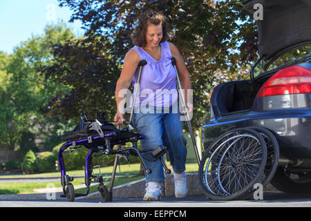 Donna con la Spina Bifida usando stampelle per prendere la sedia a rotelle oltre che per i viaggi in auto Foto Stock