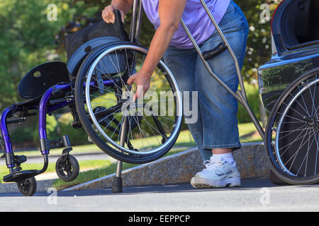 Donna con la Spina Bifida usando stampelle per mettere insieme sedia a rotelle dopo un viaggio in auto Foto Stock
