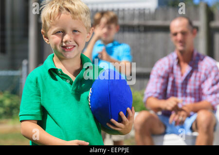 Felice ragazzo con il padre e il fratello con problemi di udito a giocare a calcio in cortile Foto Stock