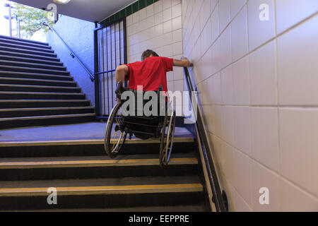 Alla moda uomo con una lesione del midollo spinale in sedia a rotelle scendendo le scale della metropolitana indietro Foto Stock