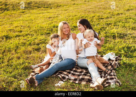 Due giovani donne con bambini godendo il sole nel parco. Bella donna incinta con il suo amico e i loro bambini. La festa della mamma conce Foto Stock