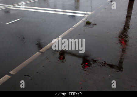 Pozza su asfalto bagnato e la riflessione di rosso semaforo Foto Stock