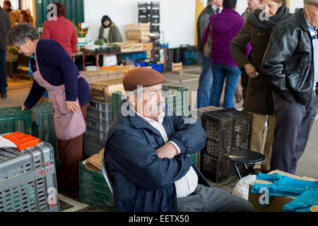 Uomo maturo seduto alla sua stalla per la vendita di frutta e verdura in un mercato in Portogallo Foto Stock