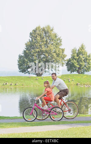 Padre e figlia equitazione biciclette presso un parco Foto Stock