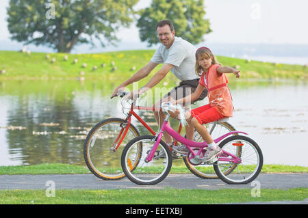 Padre e figlia equitazione biciclette presso un parco Foto Stock