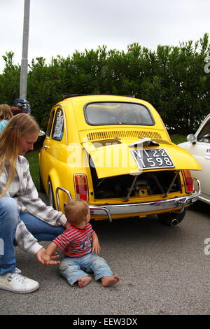 Un bambino con sua madre seduta di fronte a un giallo Fiat 500 su un carshow a Cavallino Treporti, Italia Foto Stock