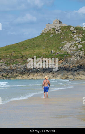 St Ives, Cornovaglia: l uomo è cappello di paglia a piedi lungo Porthmeor Beach di St Nicholas' Cappella in background Foto Stock