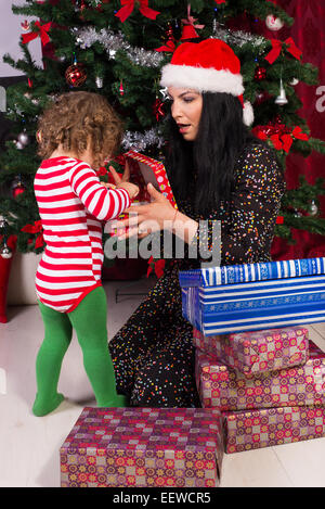 Stupito la madre e il bambino ragazzo di aprire i regali di Natale sotto agli alberi Foto Stock