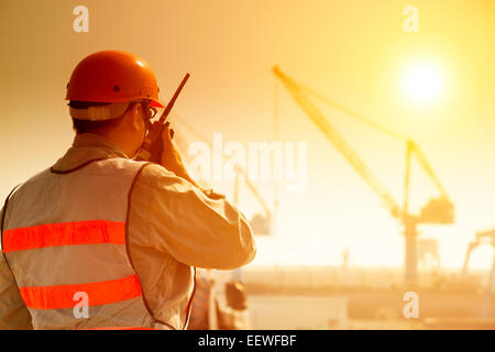 Lavoratore con grande gru sito e sfondo al tramonto Foto Stock