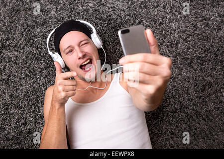 Attraente uomo con le cuffie in una camicia bianca rende selfie con il suo telefono cellulare Foto Stock