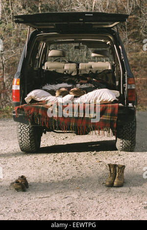 Coppia giovane dormire nel retro della loro auto, stivali in piedi sul suolo in primo piano.