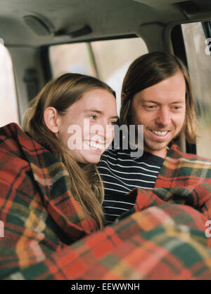 Un sorridente giovane seduto nella loro auto, coperto da una coperta. Foto Stock