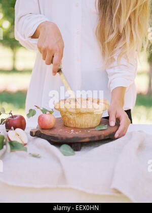 Donna in piedi a un tavolo di taglio di una fetta di torta di mele. Foto Stock