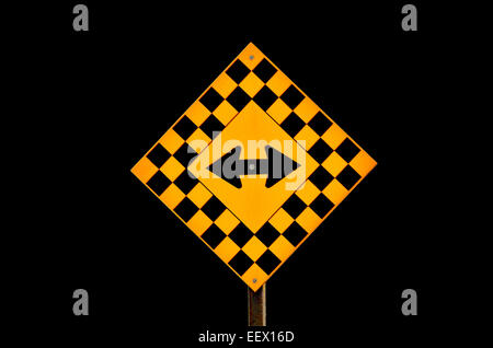 Un nero e giallo autostrada segno con una freccia che mostra due modi di viaggiare su uno sfondo nero. Foto Stock