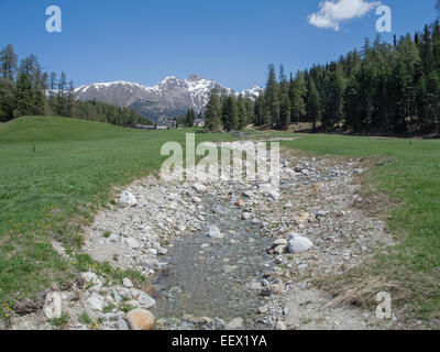 Paesaggio vicino a St. Moritz in Svizzera che mostra un piccolo ruscello e sfondo di montagne innevate contro un cielo blu Foto Stock