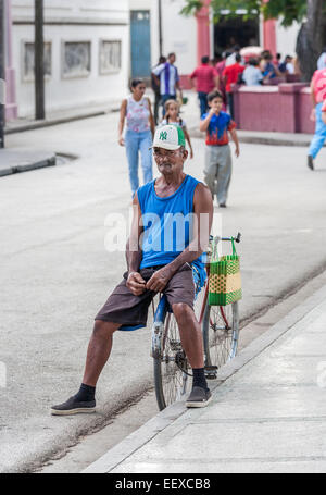 Stile di vita a Cuba: Locale uomo cubano a Camaguey, Cuba è la terza più grande città, indossando una parte superiore blu e pantaloncini, seduto su una bicicletta Foto Stock