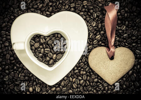 Caffè il concetto di tempo. Cuore di coppa a forma di piastra e cookie gingerbread su i chicchi di caffè sfondo. Vista superiore Foto Stock