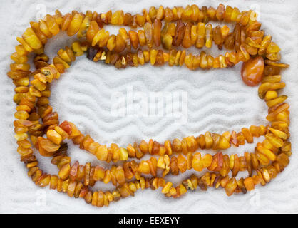 La collana di ambra grezza giace sul puro bianco sabbia di mare. Sfondo di macro Foto Stock