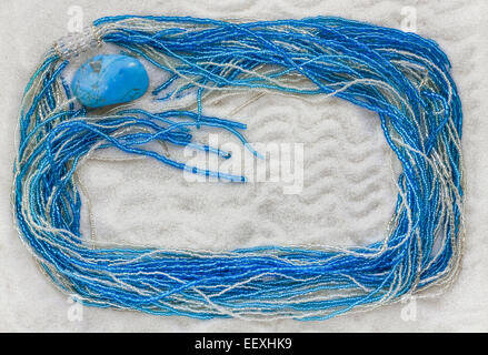 La collana dal blu e argento perle di vetro giace sul puro bianco sabbia di mare. Sfondo di macro Foto Stock