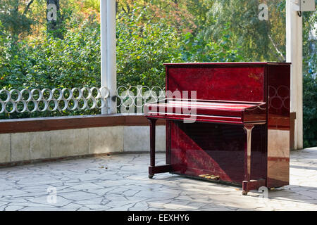 In attesa del concetto di musica. Il vecchio graffiato rosso pianoforte su una scena nel parco della città. Soleggiato al mattino di autunno Foto Stock