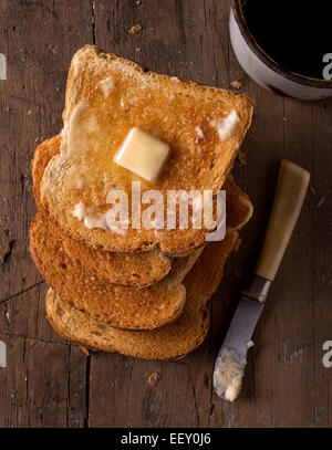 Crostini di pane tostato imburrato le fette su un piano portapaziente rustico con caffè. Foto Stock
