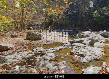 Un uomo dà dei calci indietro su una grande roccia e orologi a scenic, rocciosa, fiume di montagna rullo dal bosco circostante in autunno Foto Stock