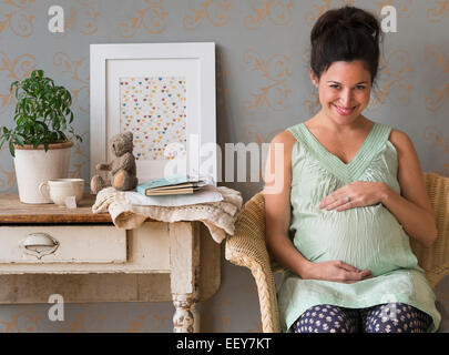 Donna incinta seduto nella sedia toccando addome sorridente Foto Stock