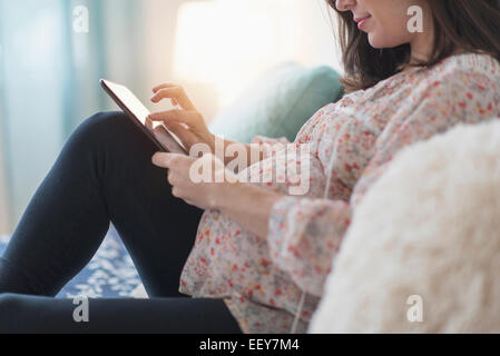 Donna incinta seduta sul letto tramite tablet Foto Stock
