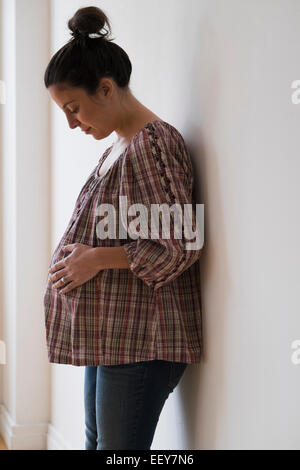 Donna incinta appoggiata contro la parete Foto Stock