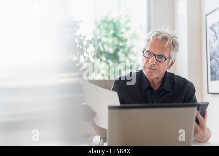 Senior uomo seduto in casa e ufficio con computer portatile Foto Stock