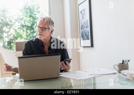 Senior uomo seduto in casa e ufficio con computer portatile Foto Stock