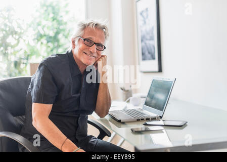 Ritratto di sorridere senior uomo seduto in home office Foto Stock