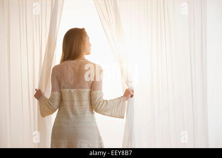 Giovane donna apertura tende in mattinata Foto Stock